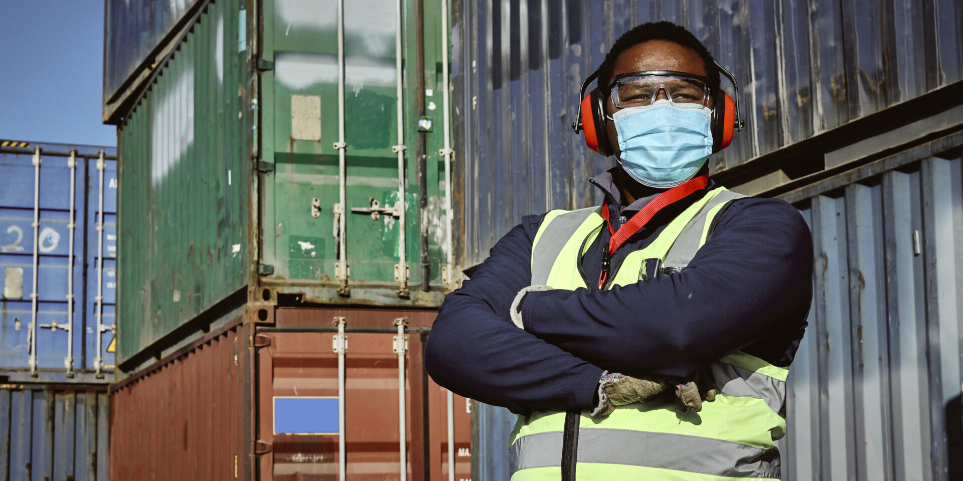 A man assessing and accounting for shipping containers in a storage yard in Johannesburg South Africa. He is wearing a reflective vest and a face mask.