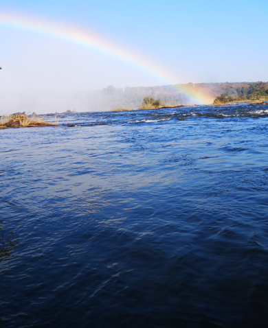 Image of a flowing river with a rainbow in the sky.