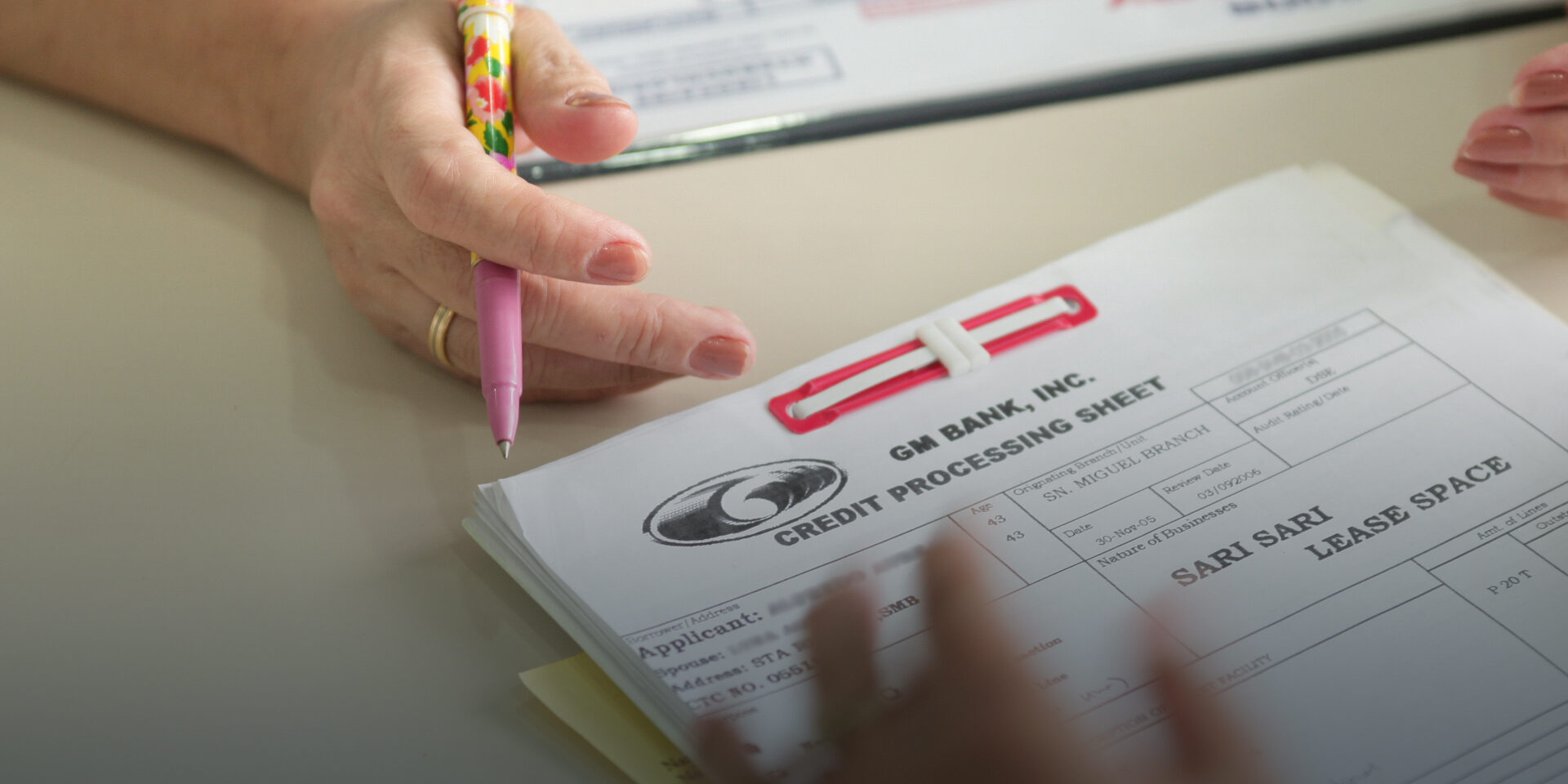 A close-up image of a credit processing form with a hand holding a pen above it.
