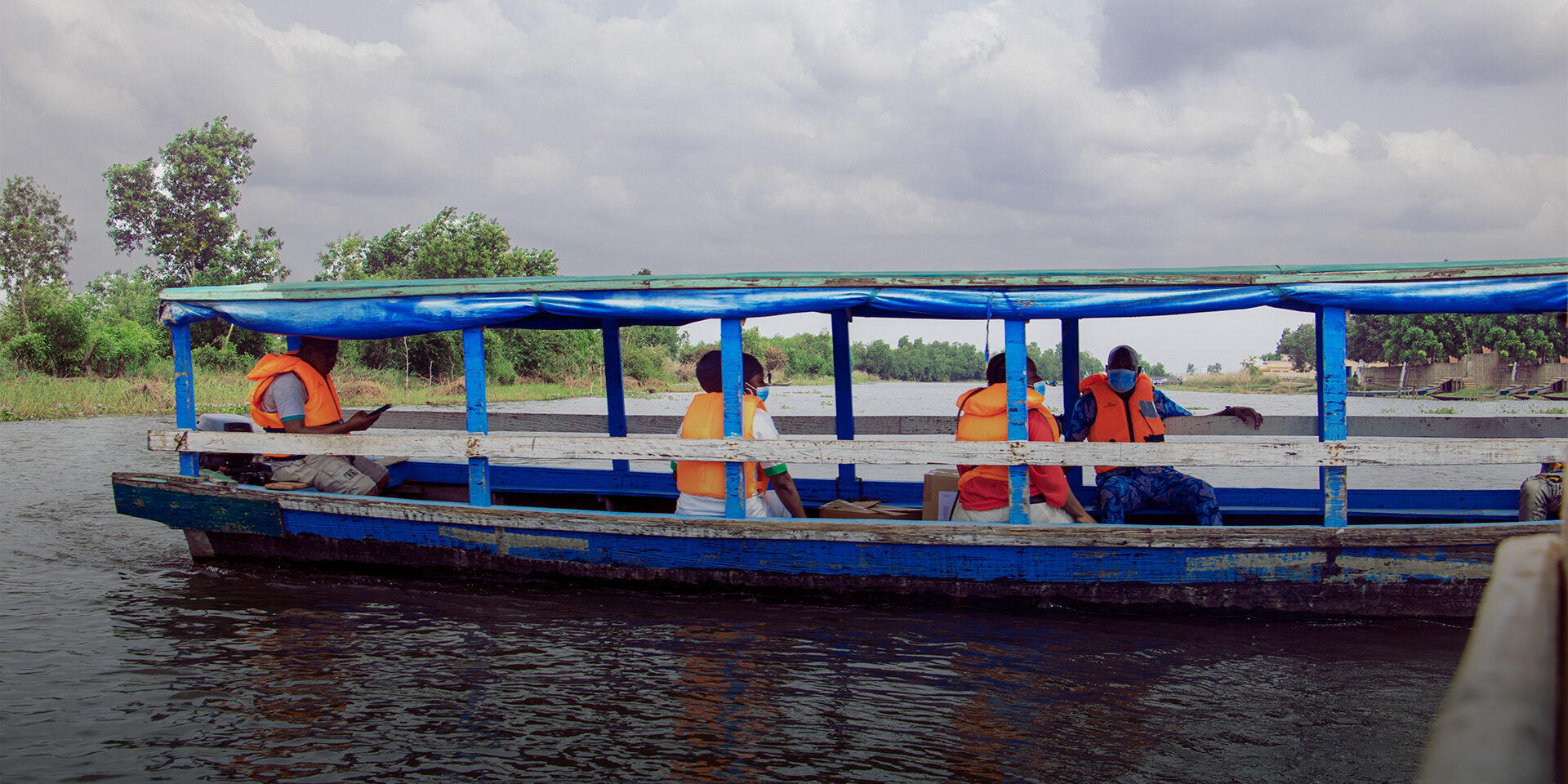 Image of a blue boat going down a river with five passengers.