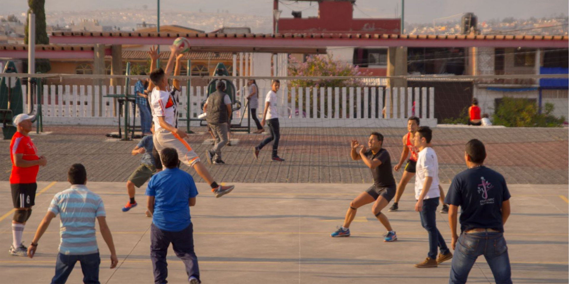 Several young adults playing volleyball on a concrete playing surface.
