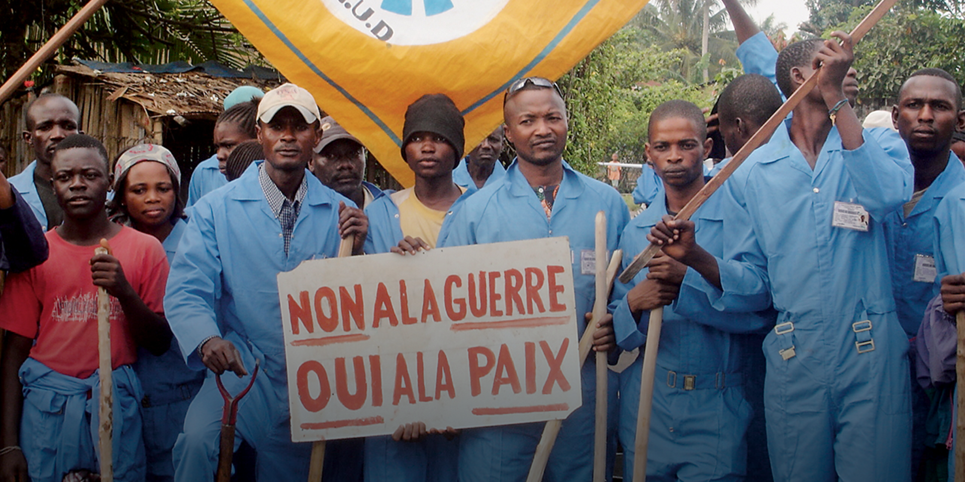 A group of men dressed in blue hold a sign asking for peace