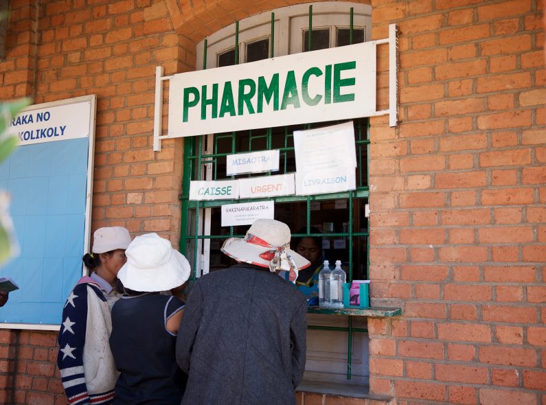People standing at the window of a pharmacy being served by a technician.