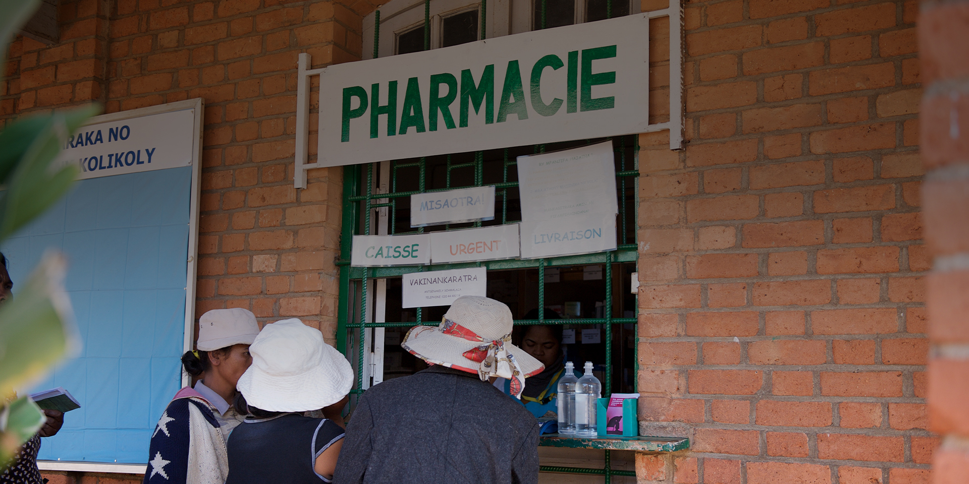 People standing at the window of a pharmacy being served by a technician.