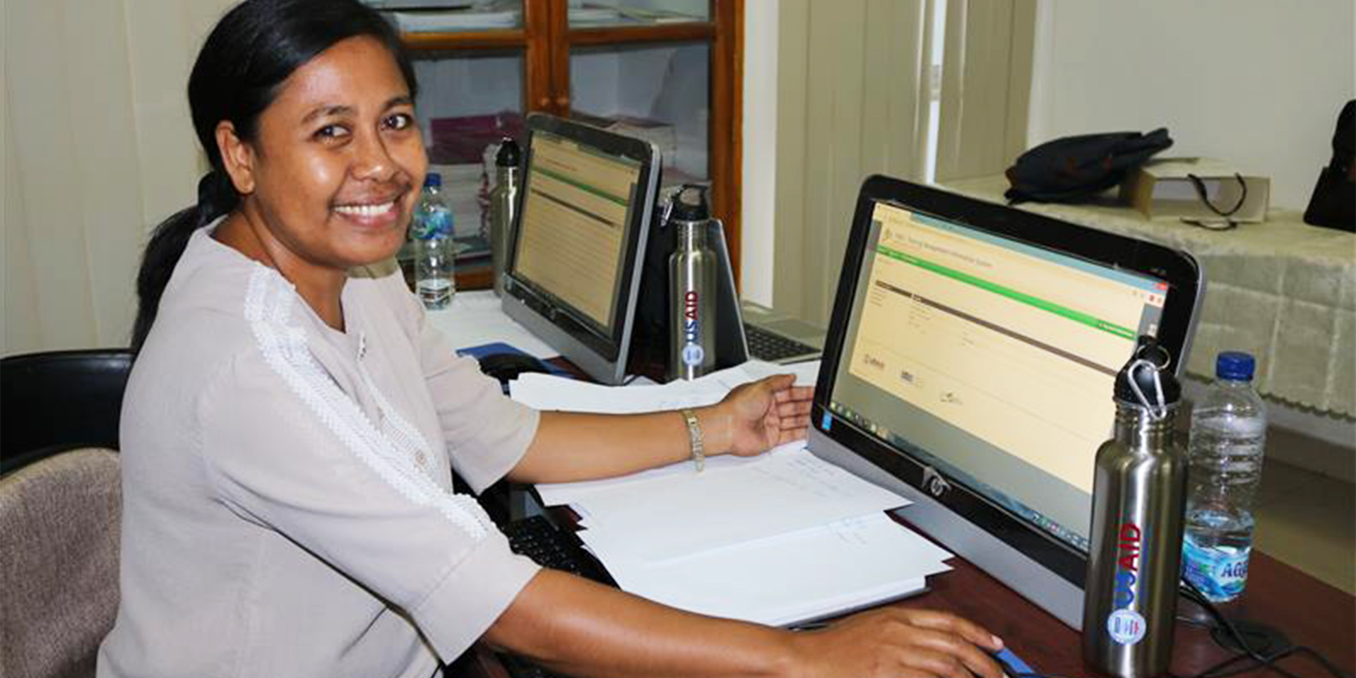 A woman sitting at a table working on a computer and smiling.