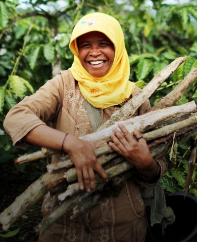 A woman smiling as she carries a bundle of sticks.