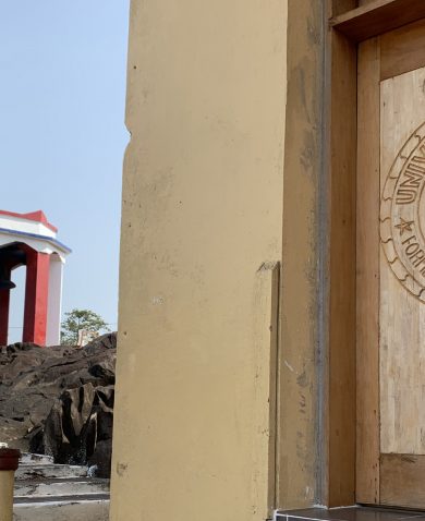 Image of the logo for the University of Liberia carved into wood on a door. Beside it is a stairway leading up to a gazebo.