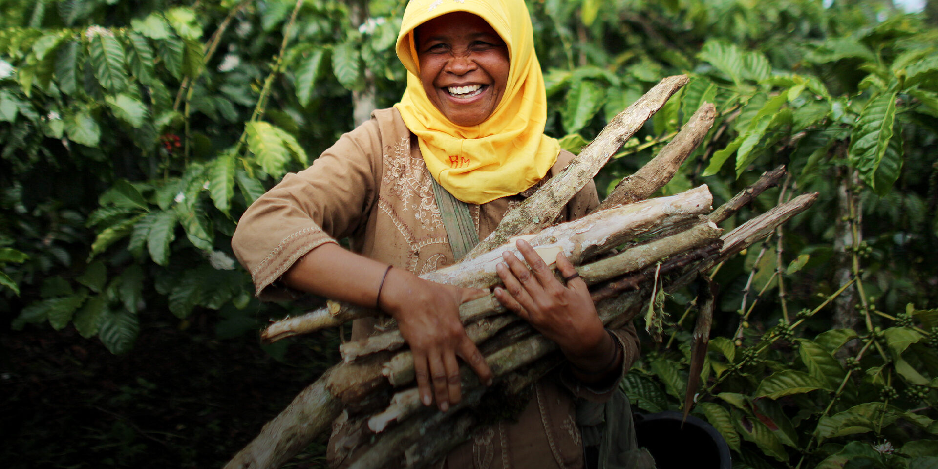A woman smiling and carrying a bundle of sticks.