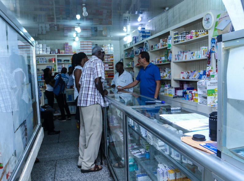 The inside of a pharmacy as patients speak to a vendor across a glass display case.