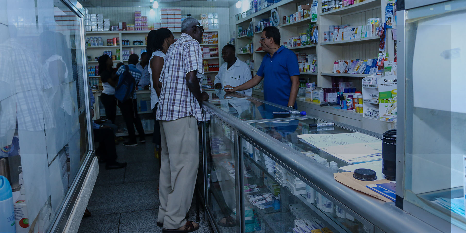 The inside of a pharmacy as patients speak to a vendor across a glass display case.
