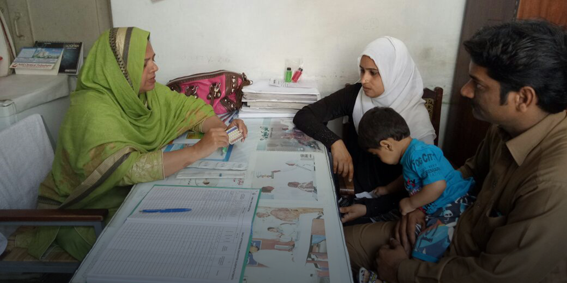 A woman sitting across a table from a family and explaining the use of medicine she is presenting to them.