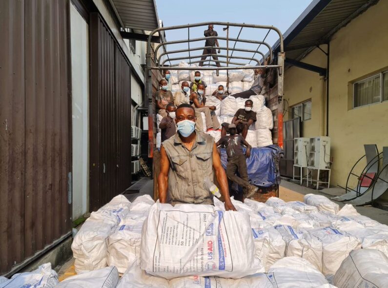 A group of people posing for a photo as they load large white sacks marked "USAID" onto a truck.