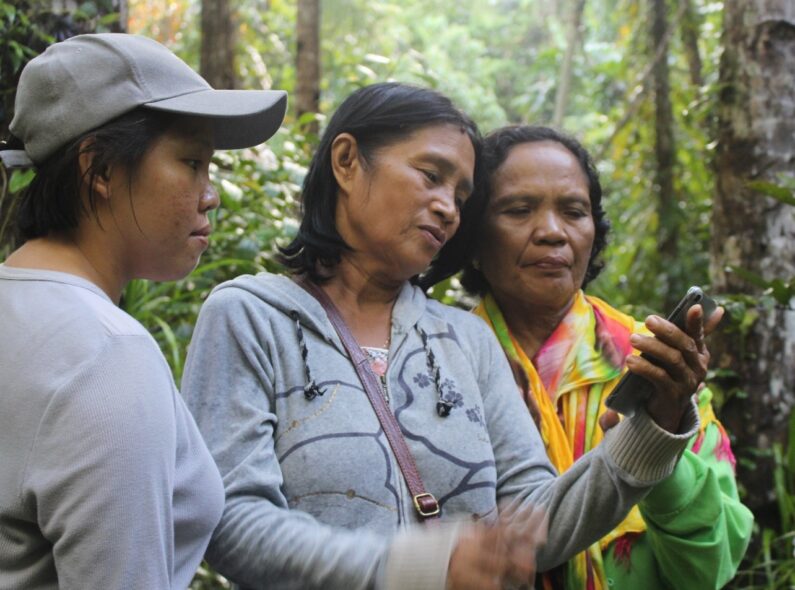 Three women standing in a forest and looking at a smartphone.