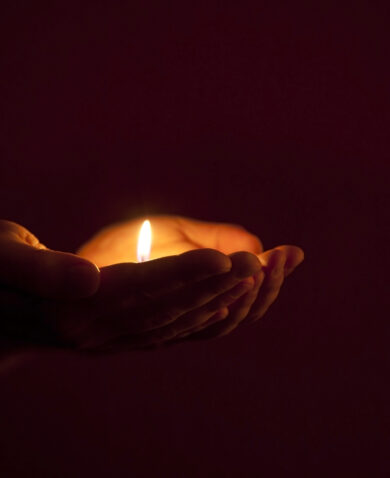 A pair of hands holding a tea candle in the darkness.