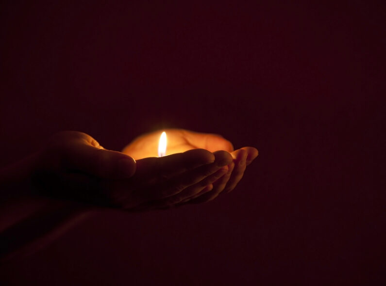 A pair of hands holding a tea candle in the darkness.