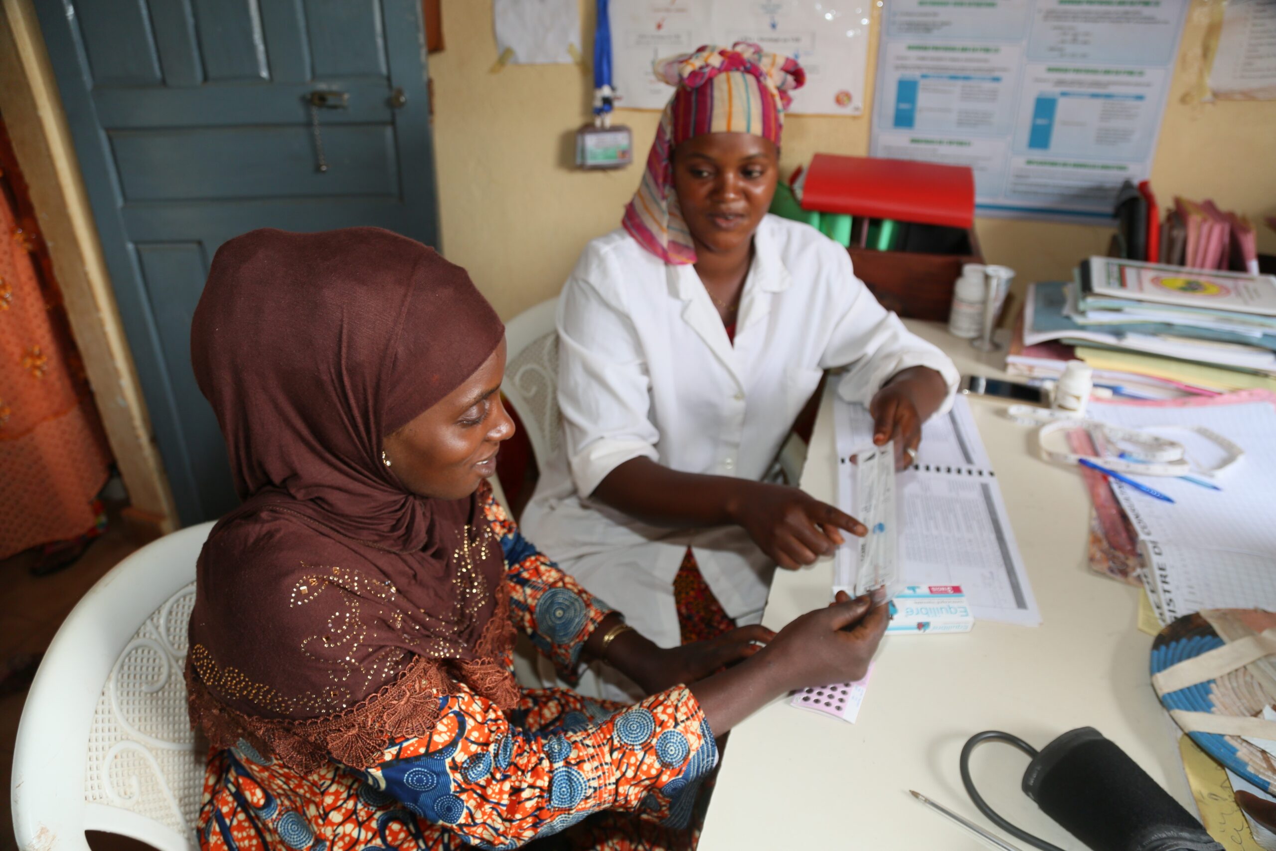 A female pharmacist sitting with a female patient during a family planning counseling session. The pharmacist is explaining the use of a device to the patient.