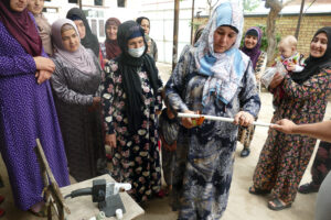 A woman holds a plastic water pipe, while standing with a group of women during a plumbing class.