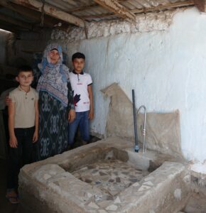 A woman with her two young boys stands next to the water stand she built in her home.