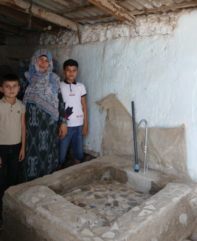 Woman and two boys stand next to water basin she constructed in her home.