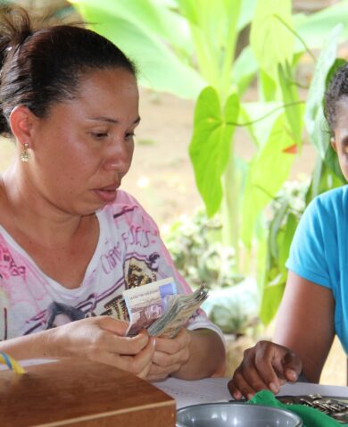 Two women in Colombia sit at an outdoor table, counting money.