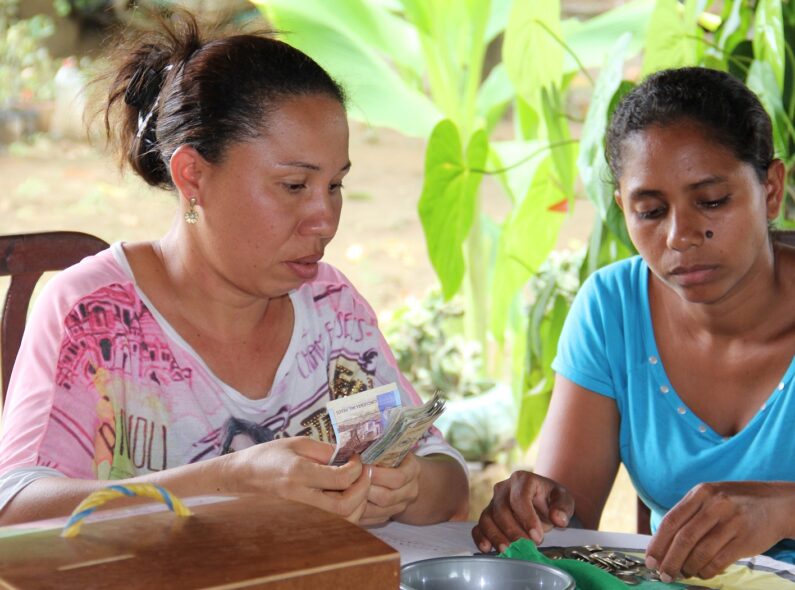 Two women in Colombia sit at an outdoor table, counting money.