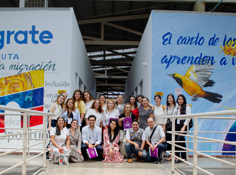 Group of people in a hallway in front of a sign that says "Integrate" with a picture of the Colombian flag.