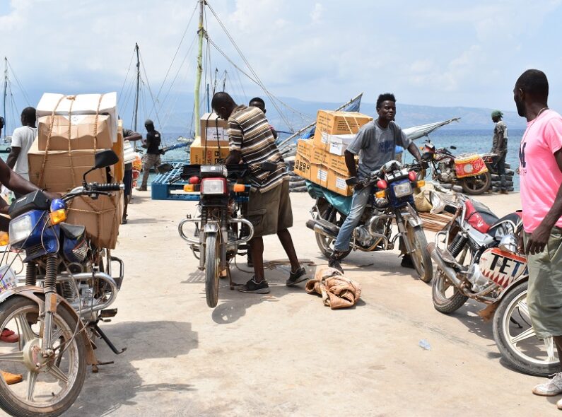 Four people standing next to a loading dock and beside motorbikes packed with cargo.