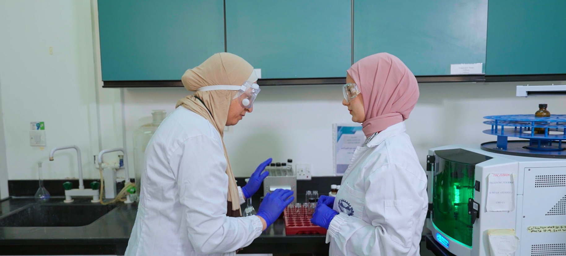 Two women in protective wear work in a lab