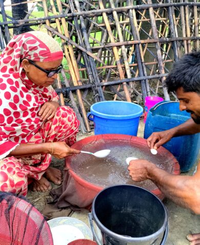 A man and a woman kneeling outside as they spoon liquid out of a large bowl.
