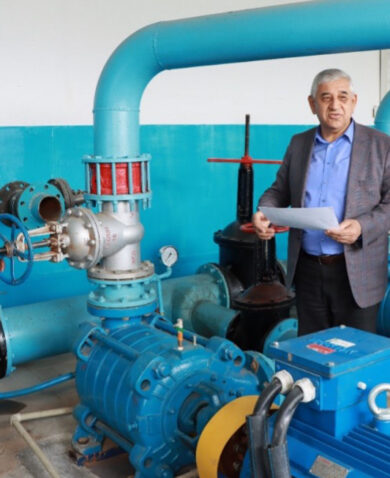 Image of a man standing next to a large blue pump with tubes and valves attached.