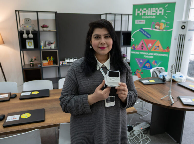 Zhela, a software engineer holds a coding tool in front of laptops