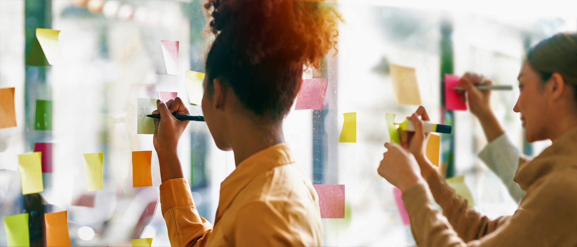 Women write on sticky notes on a wall