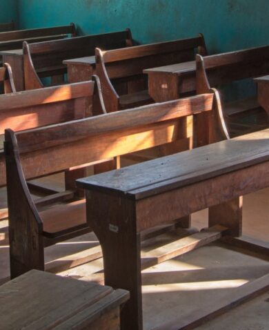 A school room full of empty benches with light shining through a window.