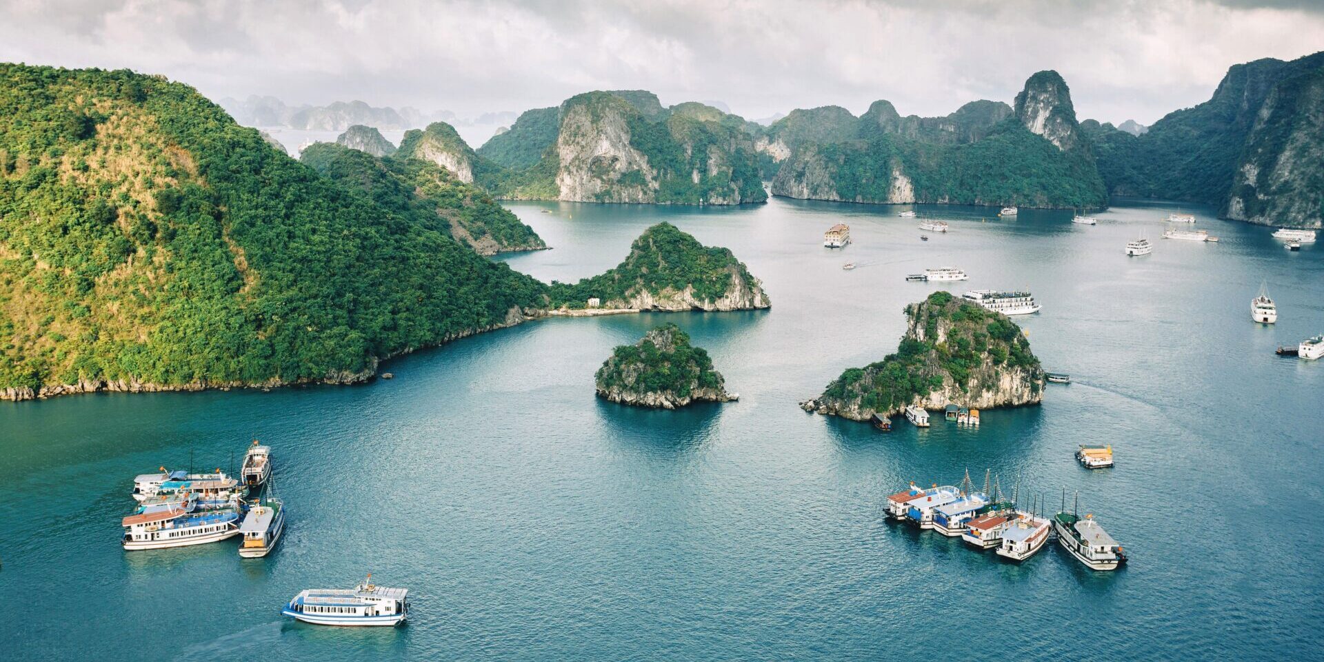 An aerial view of Halong Bay in Vietnam. Several boats can be seen traveling between green, mountainous islands.