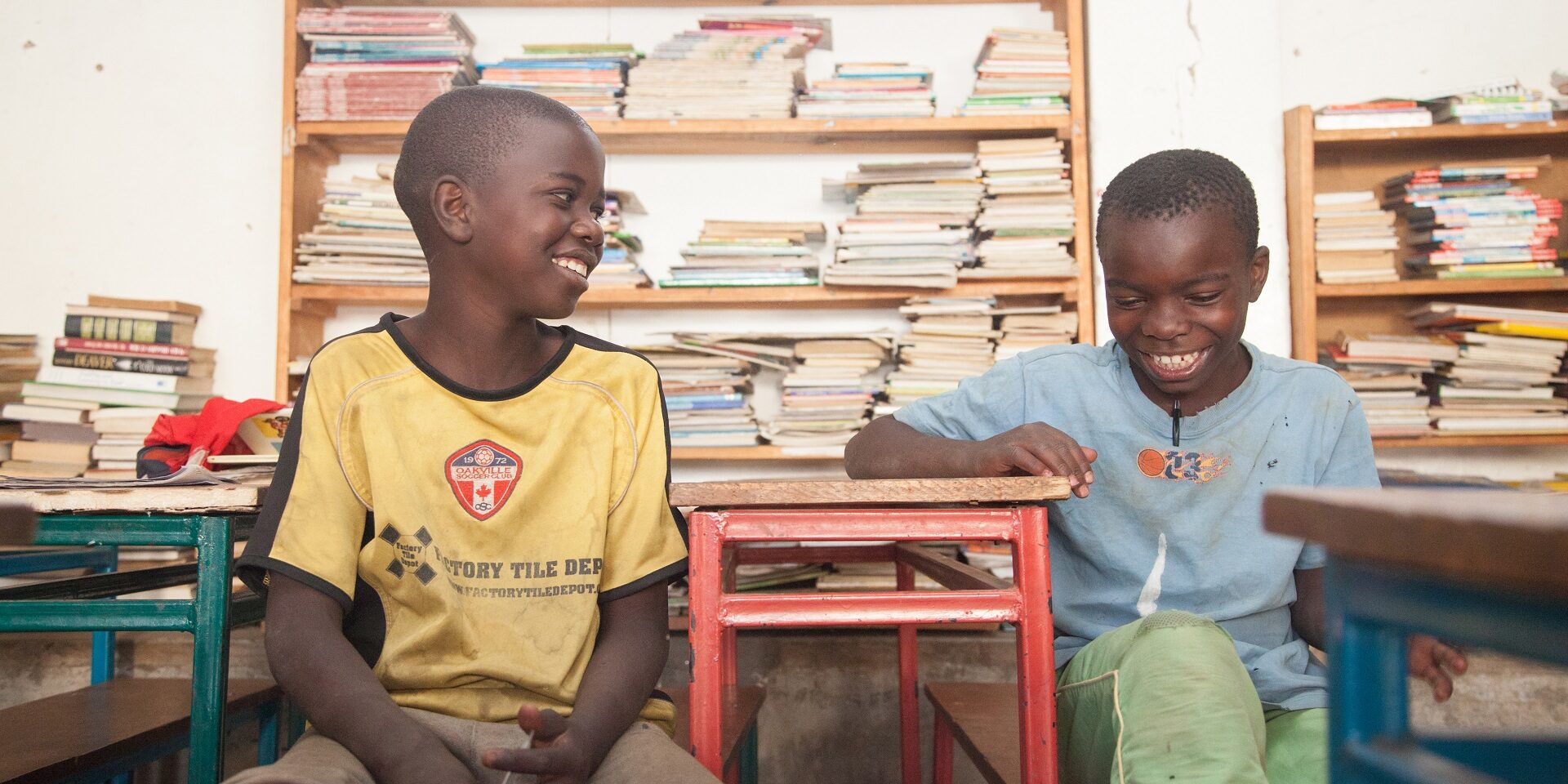 Two smiling schoolboys in Zambia sitting in front of bookshelves
