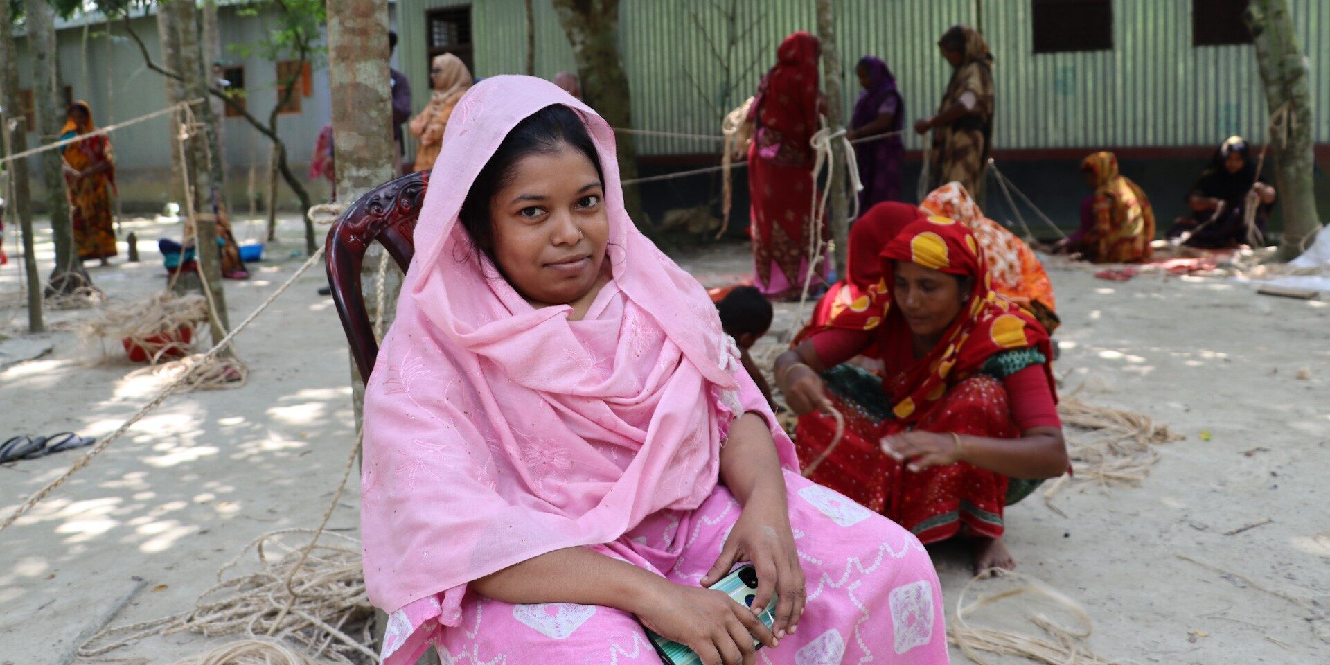 Subarna Khatun sits cross-legged on the ground outside, in front of a group of other female artisans