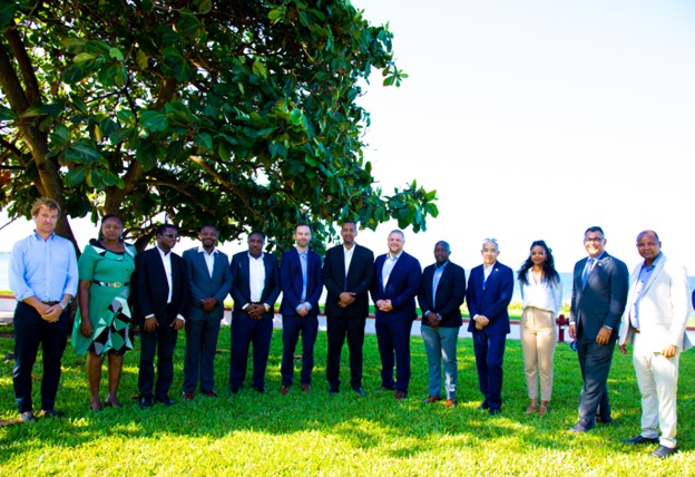 Group of Heshimu Bahari staff with Senior USAID Leadership and implementing governments standing outside on the grass in front of a tree.