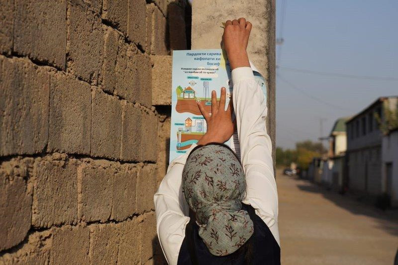 The back of a woman who is putting up a poster on water use against a brick wall.