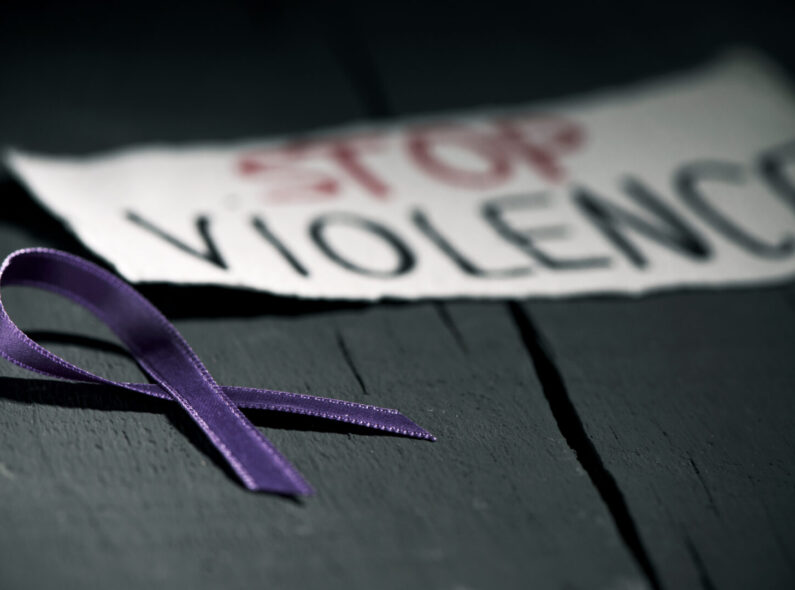 A purple ribbon and the text 'Stop Violence' on a piece of paper, on a dark gray rustic wooden surface.