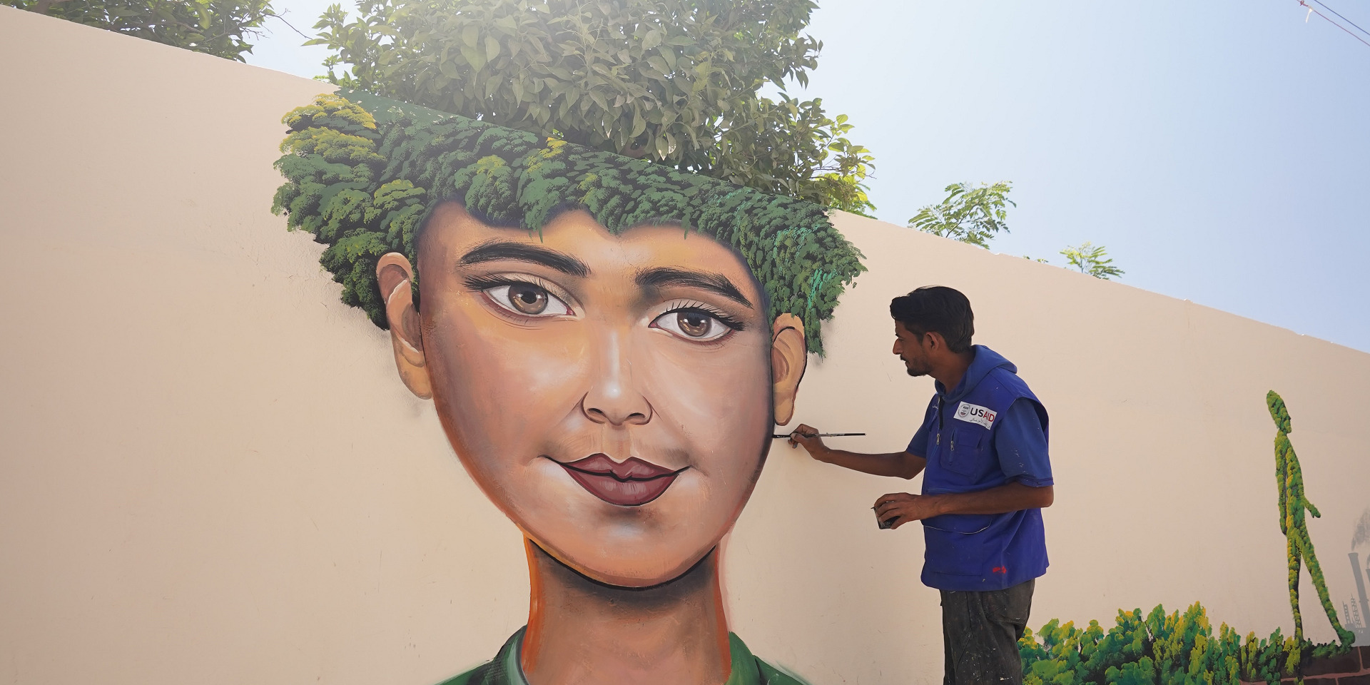 A man paints a mural of a woman's face with leaves for hair.
