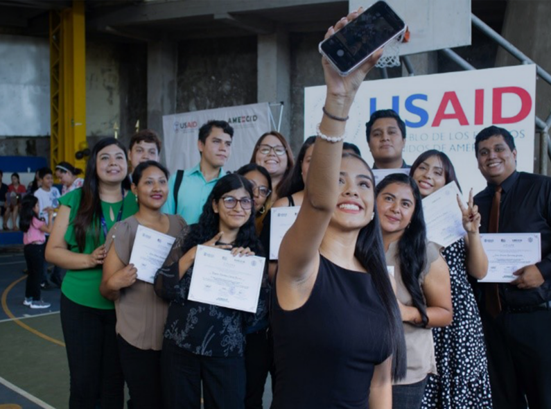 Large group of students taking a selfie, holding diplomas in their hand.