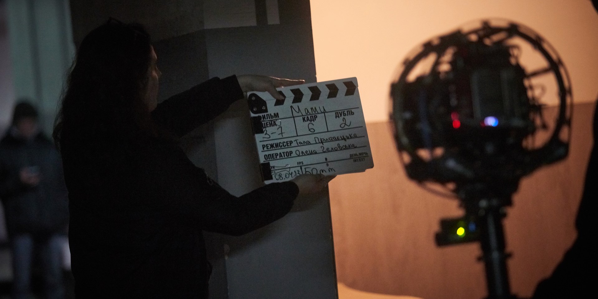 Behind the scenes of the Ukrainian drama series, Those Who Stayed. A woman stands with her back to the photographer, holding a clapper board, as they prepare to film an episode.