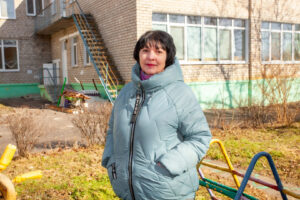 A woman, Olha Poliova, in front of a kindergarten building.