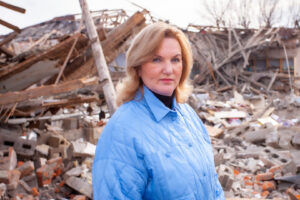 A woman, Halyna Minayeva, in front of a building's destruction. 