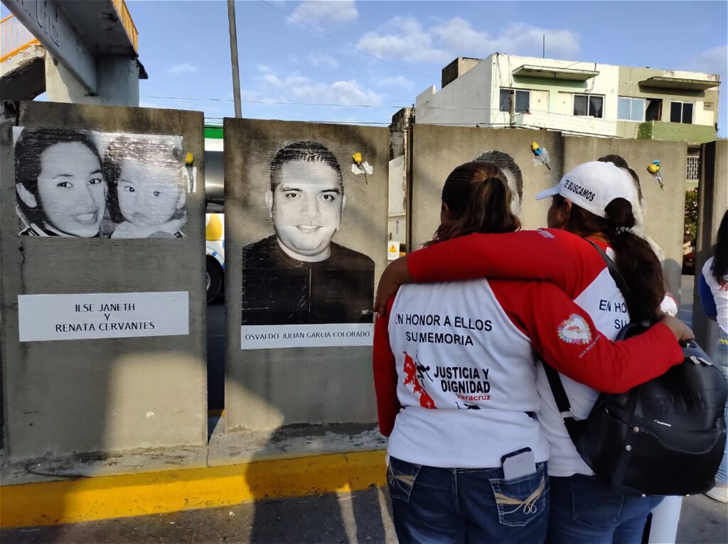 Two women stand in front of a poster of a missing person in Mexico.