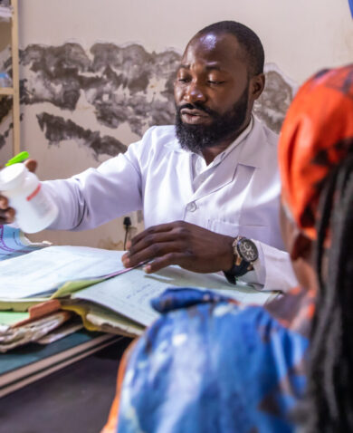 A health worker holds a bottle of HIV medicine while at his desk speaking to a woman patient