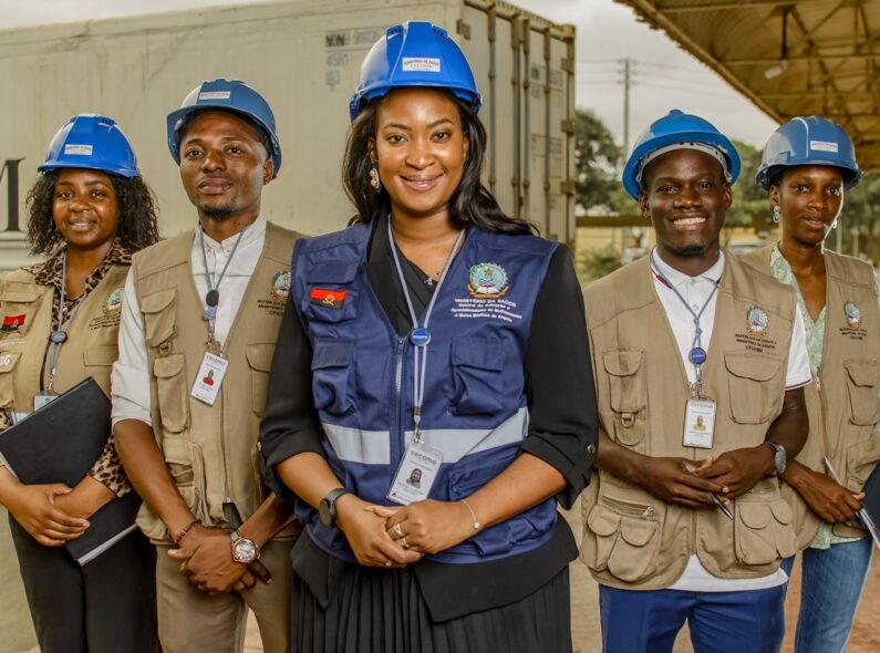 A group of people wearing hard hats and safety jackets stand in front of a CECOMA truck