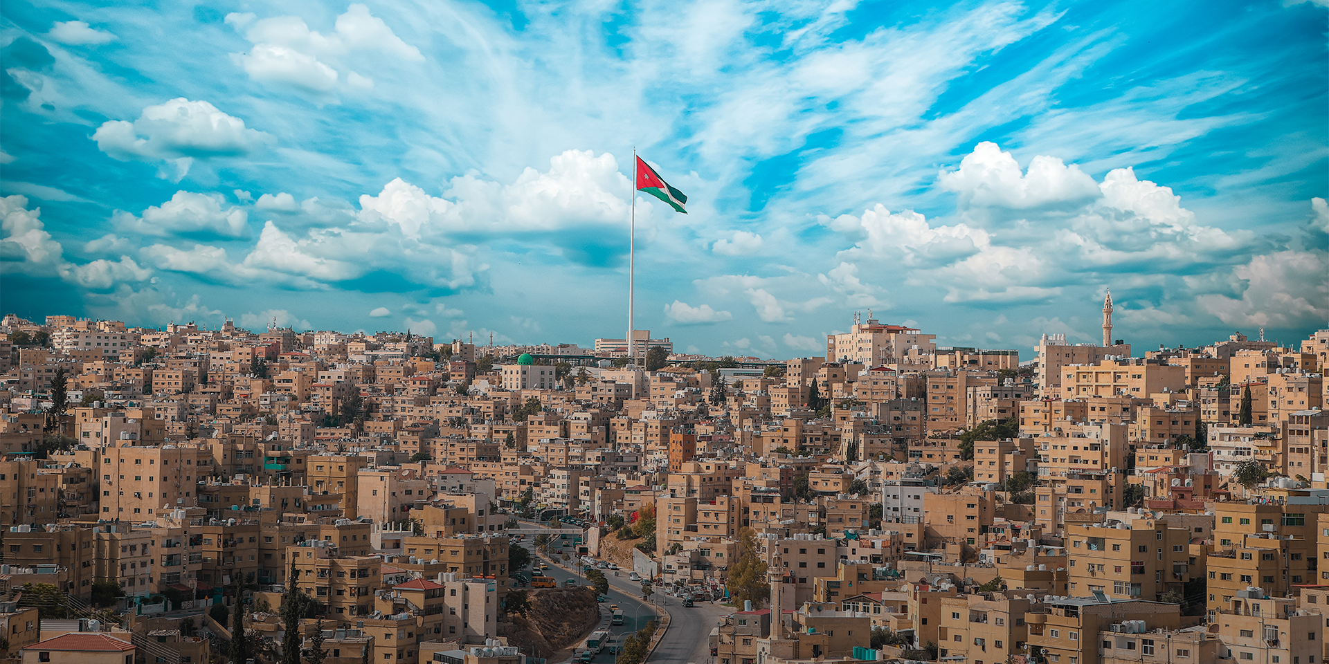 A panoramic view of Amman with a Jordanian flag raised in the middle. 