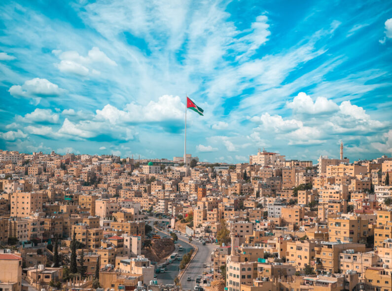 A panoramic view of Amman with a Jordanian flag raised in the middle. 