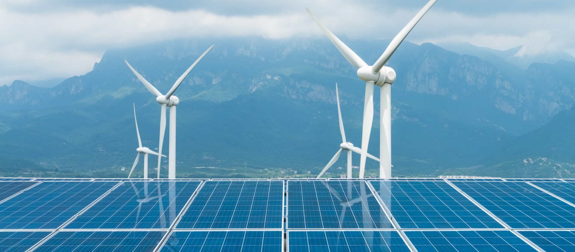 photo of solar panels and wind mills with mountains in the background